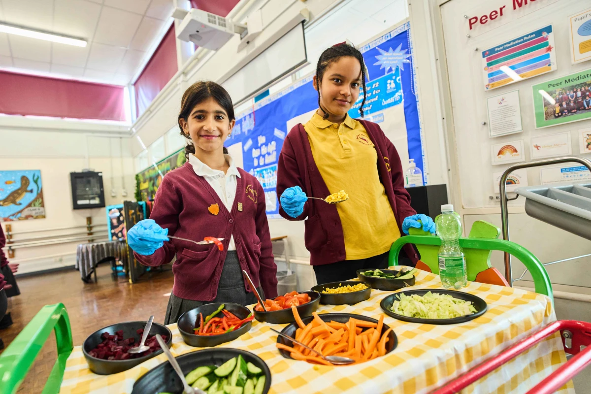 PHC London-Healthy Foods 2025. Image of two schoolgirls serving vegetables from a buffet cart